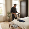 Man in a bright modern Belgian bedroom compares neatly folded men's underwear on a bed, showing fit, fabric and everyday comfort.